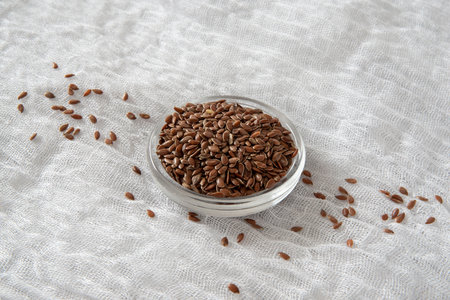 flax seeds in a glass bowl on a white fabric background.の写真素材