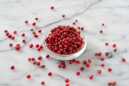 Red peppercorns in a glass bowl on a white marble backgroundの写真素材