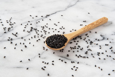 Black sesame seeds in a wooden spoon on white marble background.の写真素材