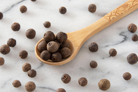 Wooden spoon full of allspice on white marble background.の写真素材