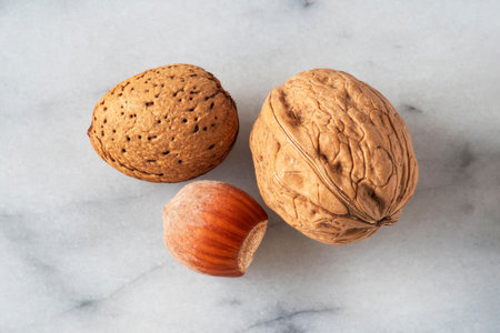 Close-up of almonds, walnuts and hazelnuts with their shells on white marbleの写真素材
