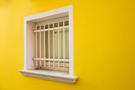White window with grille on a yellow wall, Caorleの写真素材