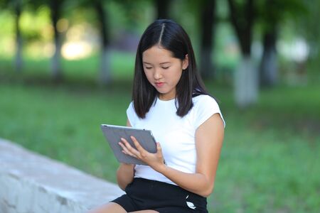 Girl female teenager with black hair in a bob white east Asian woman green park background. Lady holding plate and presses a finger, smiling, looking into the camera.の写真素材