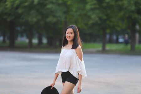 female nature keeps his hat summer sun sunset looks pleased. azitka woman black hair white shirt black shorts out trees around.の写真素材