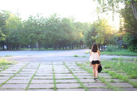 female nature keeps his hat summer sun sunset looks pleased. azitka woman black hair white shirt black shorts dancing around the trees looking at the camera. portrait. spinningの写真素材