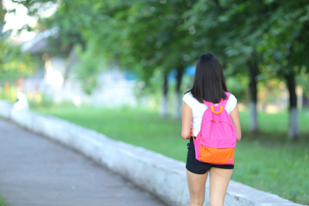 Girl female teenager with black hair in a bob white east Asian woman green park with a backpack background. Lady walking, goes, walk away, look at the camera.の写真素材