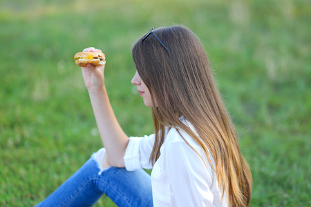 female in the park works behind laptop. beautiful girl with glasses eating fast food in nature and smiling.の写真素材