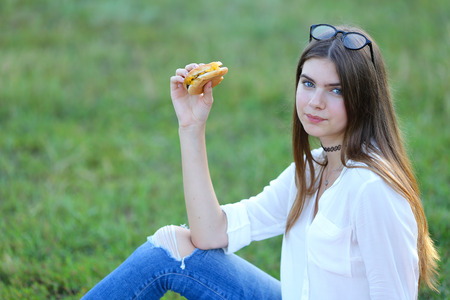 female in the park works behind laptop. beautiful girl with glasses eating fast food in nature and smiling.の写真素材