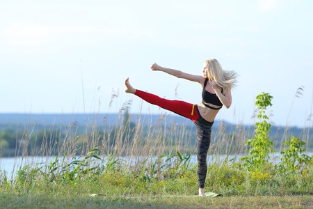 Young beautiful woman squats shows result press on stomach workout training wearing top. Blonde female long hair doing exercises engaged in sports be fit, strong form green background nature park.の写真素材
