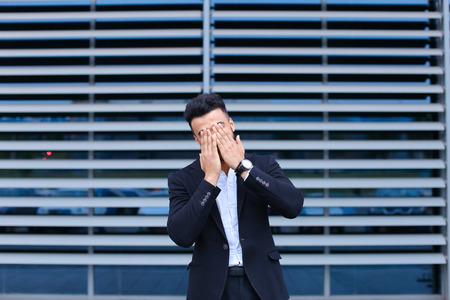 Entrepreneur shows neck pain tired looking  at the camera. Young handsome businessman arab muslims in business center wearing dressed in black elegant suit on building background.の写真素材