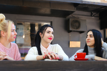 Concept female friendship, meeting, lunch. Three beautiful women sitting incafe smiling, talking, telling secrets, drink coffeeの写真素材