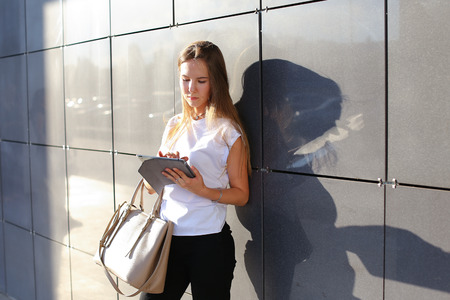 Female work, negotiating, solves problems, browsing touch looking tablet. Young beautiful business woman entrepreneur with long hair wearing suit standing near center technology sun.の写真素材