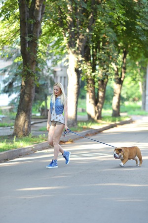 Young beautiful woman girl lady blond hair with red lips in casual style american bulldog. Woman plays with dog glad, laughing, happy and inspired walking goes.の写真素材