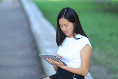 Girl female teenager with black hair in a bob white east Asian woman green park background. Lady holding plate and presses a finger, smiling, looking into the camera.の写真素材