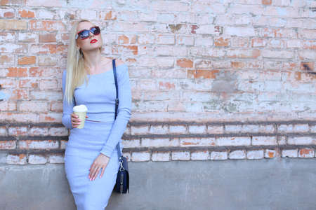 Woman blond hair slim athletic figure near brick wall stands wearing sunglasses.の写真素材