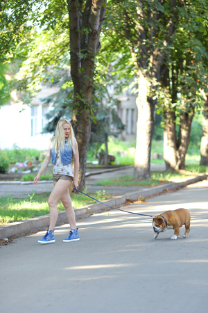 Young beautiful woman girl lady blond hair with red lips in casual style american bulldog. Woman plays with dog glad, laughing, happy and inspired walking goes.の写真素材