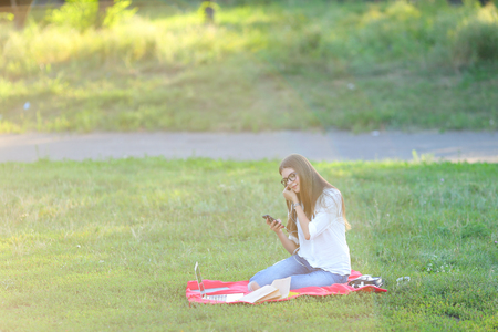 girl listening to music on the nature of the glasses. in the park for a laptop unravels headphones and holding a mobile phoneの写真素材