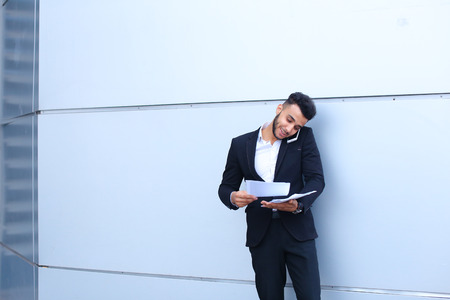 Entrepreneur man male looking at camera and smiling point hand to entrance door. Young handsome businessman arab muslims in business center wearing dressed in black elegant suit on building background.の写真素材