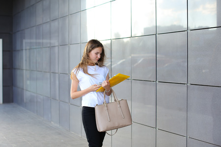 Female work, negotiating, solves problems, walking to camera holds document talking on smart phone indignant displeased. Young beautiful business woman entrepreneur with long hair wearing suit standing near center technology.の写真素材
