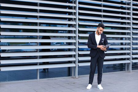 Young handsome businessman Arab Muslims is in the business center in black elegant dress on building background. Businessman man male looking waiting concept and smiling.の写真素材