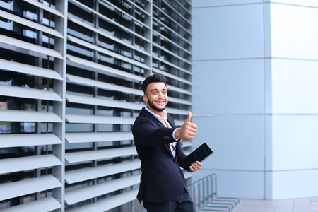 Young handsome businessman Arab Muslims is in the business center in black elegant dress on building background. Businessman man male looking waiting concept and smiling.の写真素材