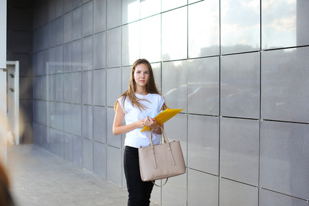 Female work, negotiating, solves problems, walking to camera holds document talking on smart phone indignant displeased. Young beautiful business woman entrepreneur with long hair wearing suit standing near center technology.の写真素材