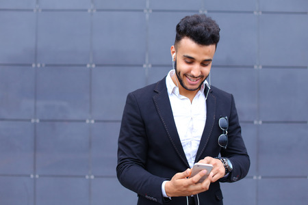 Entrepreneur man male looking at camera and smiling talks on mobile smart phone. Young handsome businessman in business center wearing dressed in black elegant suit on building background.の写真素材