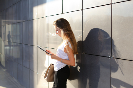 Female work, negotiating, solves problems, browsing touch looking tablet. Young beautiful business woman entrepreneur with long hair wearing suit standing near center technology sun.の写真素材