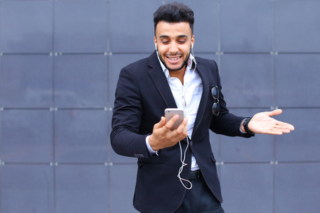 Entrepreneur takes makes selfie man male looking at camera and smiling talks on mobile smart phone. Young handsome businessman   in business center wearing dressed in black elegant suit on building background.の写真素材