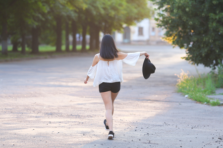 female nature keeps his hat summer sun sunset looks pleased. azitka woman black hair white shirt black shorts out trees around.の写真素材