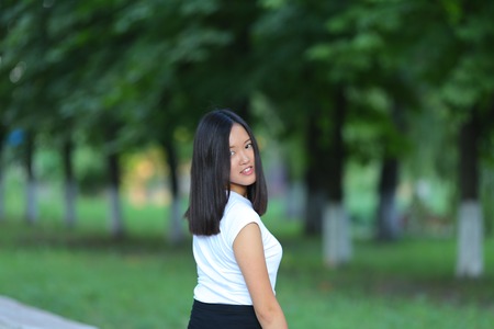 Girl female teenager with black hair in a bob white east Asian woman green park with a backpack background. Lady holds, dials, push your finger, smiling, looking into the camera, talking on the phone happy portrait.の写真素材