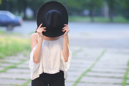 female nature keeps his hat summer sun sunset looks pleased. azitka woman black hair white shirt black shorts dancing around the trees looking at the camera. portrait. spinningの写真素材