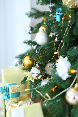 Christmas tree decorated with balls, silver ribbons, pine cones and garland of snowflakes beside lying gift boxes with blue ribbons. Concept of christmas tree, new year eve, holidays, winter.の写真素材
