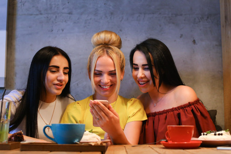 Concept female friendship, meeting, lunch. Three beautiful women sitting in cafe smiling, talking, telling secrets, eat, drink coffeeの写真素材