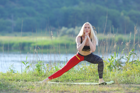 Young beautiful woman shows press stomach workout training wearing top. Blonde female long hair squats weighted arm legs exercises engaged in sports be fit, strong form green background nature park.の写真素材