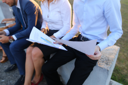 Young contemporary confident people, two boys and two girls, perspective entrepreneurs, students smiling, chatting with each other, using gadgets, laptops, tablet and smartphone for work with office programs, drawing up business plan, discuss working momeの写真素材