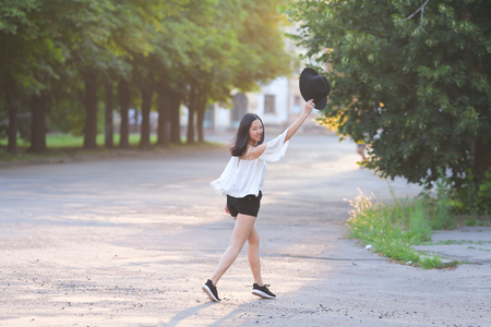 female nature keeps his hat summer sun sunset looks pleased. azitka woman black hair white shirt black shorts out trees around.の写真素材