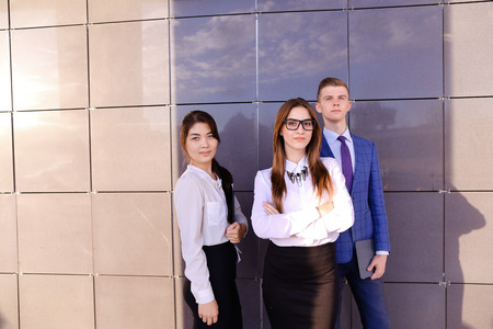 Modern handsome male man and two pretty confident girl, successful young office workers, businessmen, students holding in hands documents, smiling and posing to photographer camera, taking pictures for company brochures, advertising office clothes and staの写真素材