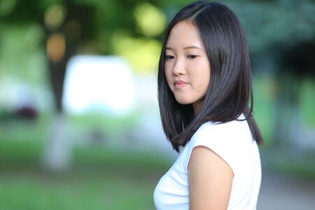 Girl female teenager with black hair in a bob white east Asian woman green park with a backpack background. Lady holds, dials, push your finger, smiling, looking into the camera, talking on the phone happy portrait.の写真素材