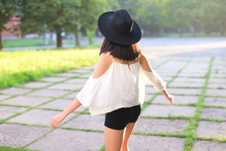 female hat nature summer sun sunset looks pleased. azitka woman black hair white shirt black shorts dancing around the trees looking at the camera. portrait.の写真素材
