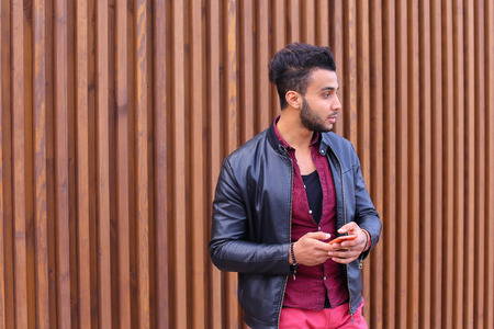 Young Arab pleasant appearance reads and writes message, smiling looking to side, makes appointment and looks forward to important person, smiling guy posing and shooting for advertising mens contemporary clothing or mobile phone brand mobile phone operatの写真素材