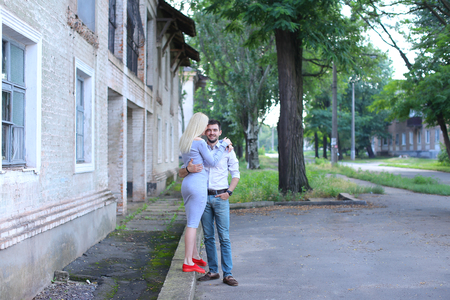 Girlfriend and boyfriend standing next to each other, posing, talking and laughing, hugging on street. Girl dressed in midi gray dress and red slip-on, guy straight, keeping hands in pants pockets and looking directly into camera, he dressed in blue jeansの写真素材