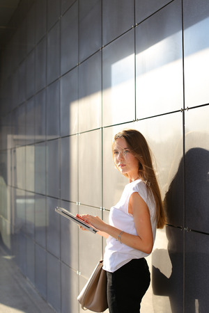 Female work, negotiating, solves problems, browsing touch looking tablet. Young beautiful business woman entrepreneur with long hair wearing suit standing near center technology sun.の写真素材