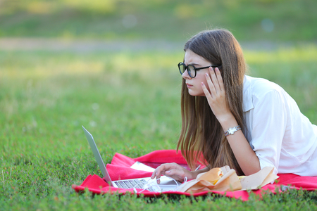 female in the park works behind laptop. beautiful girl with glasses eating fast food in nature and smiling.の写真素材