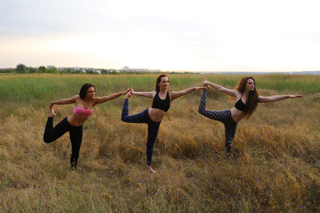 Female performing warm-up exercises and stretching, focus on correct posture execution, photographed for advertising of catalog womens sportswear or sports complex in wide field outdoors. Girl with shoulder-length hair dressed in pink top and black legginの写真素材