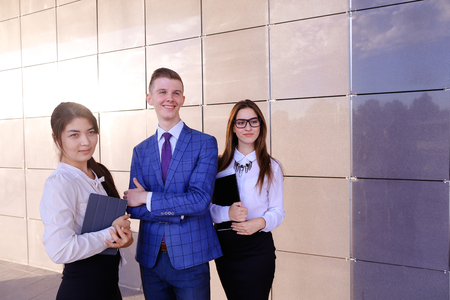Modern handsome male man and two pretty confident girl, successful young office workers, businessmen, students holding in hands documents, smiling and posing to photographer camera, taking pictures for company brochures, advertising office clothes and staの写真素材