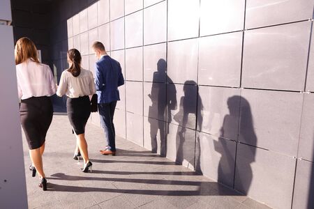 Successful male guy, businessman and two pretty young women, business people, students go in opposite direction from camera and discuss working day, returning from lunch break, study plans and kept paper in hands, graphics, and view them and go along of gの写真素材