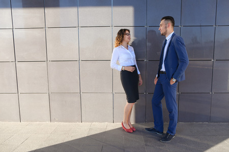 Attractive woman and man, young entrepreneurs, students and friends discuss important issues, share business ideas, smiling, laughing, make decisions, solve problems and stand next to each other near  gray wall of business center outdoors. One of guys dreの写真素材