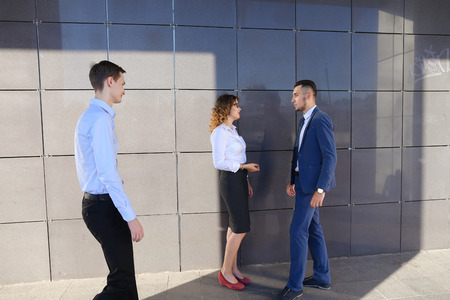 Energetic beautiful young guys and girl, businessmen and students to meet and discuss important issues, share business ideas, smiling, laughing, make decisions, solve problems and standing near gray wall of modern business center outdoors. One of guys dreの写真素材