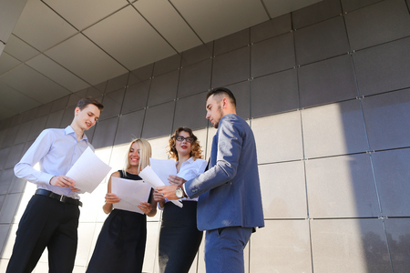 Four beautiful perspective people, two men and two women, young entrepreneurs, students, communicate, solve important problems, share of business ideas, make plans, hold in hands, consider and reading important documents, papers, smiling, laughing, posingの写真素材